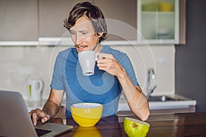 Young man having breakfast and using laptop on the kitchen