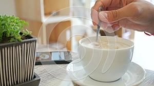 Young Man Having a Coffee Break, He is Stirring His Vegan Latte with a Spoon and Using a Mobile Phone, Hand close up. HD