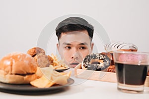 Young man having cravings for donuts, hamburger, chicken with fries instead photo