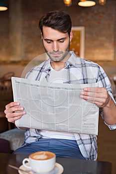 Young man having cup of coffee reading newspaper