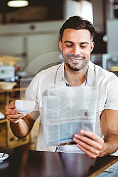 Young man having cup of coffee reading newspaper