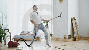 Young man having fun cleaning house with vacuum cleaner dancing like guitarist