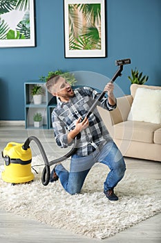 Young man having fun with vacuum cleaner while removing dirt in flat