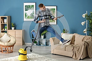 Young man having fun with vacuum cleaner while removing dirt in flat