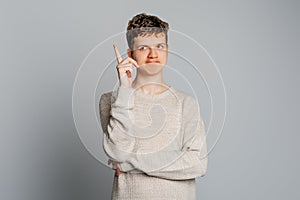 Young man having an idea. Teenager boy raised forefinger and remembers something important, standing over gray background