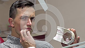 Young man having toothache, sitting in dental chair at the clinic