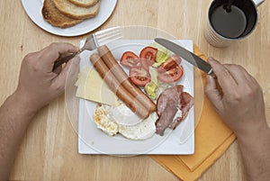 A young man is having a traditional english breakfast with bacon and eggs. Top view. Wooden table.
