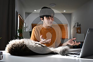Young man having videoconference with business partner while sitting with his cat at home.