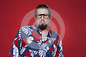 Young man in Hawaiian shirt making a face against red background