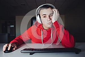 A young man in headphone use computers at night. Gamer plays games on the computer