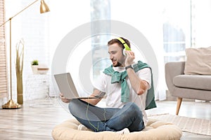 Young man with headphones and laptop sitting on floor