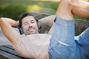 young man with headphones lying on park bench outdoors