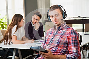 Young man in headphones and microphone with collegues in office