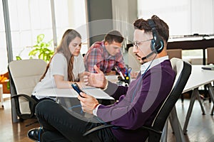 Young man in headphones and microphone with collegues in office