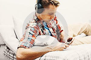 Young man in headphones with mobile phone relaxing home