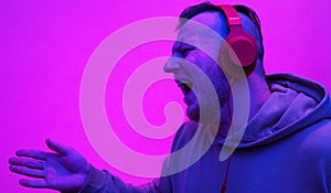 A young man in headphones sings a song on a pink background, a man listens to music in red over-ear headphones.