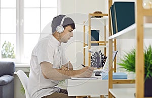 Young man in headphones studying or working online at his desk with laptop at home