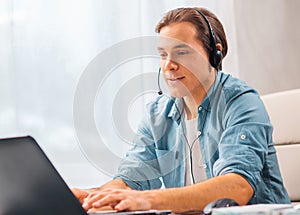 Young man in a headset works at a laptop computer. Freelancer, remote worker or student workplace. Distant work concept.