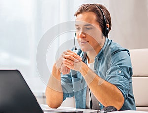 Young man in a headset works at a laptop computer. Freelancer, remote worker or student workplace. Distant work concept.