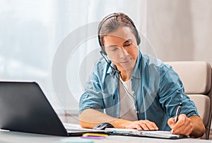 Young man in a headset works at a laptop computer. Freelancer, remote worker or student workplace. Distant work concept.