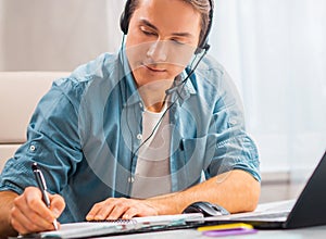Young man in a headset works at a laptop computer. Freelancer, remote worker or student workplace. Distant work concept.