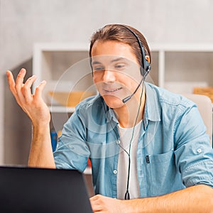 Young man in a headset works at a laptop computer. Freelancer, remote worker or student workplace. Distant work concept.