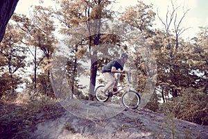 Young man in helmet training outdoors in forest, riding bmx bike, doing tricks. Autumn ride, extreme man