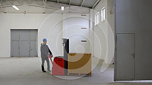 Young man in helmet, worker in warehouse checking and transporting first palette through door to empty hall. Stock of Parcels with