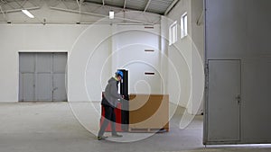 A young man in a helmet, a worker in a warehouse, checking and transporting the last pallet through the door and emptying the hall