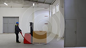 A young man in a helmet, a worker in a warehouse, transporting the last pallet through the door and emptying the hall. A warehouse