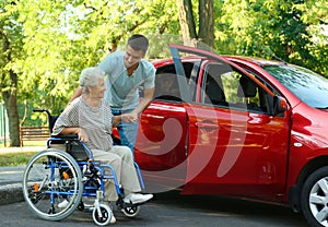 Young man helping disabled senior woman in wheelchair to get into car