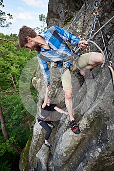 Young man helping girl climbing rocky mountain top. Helping hand. Summer extreme activities concept.