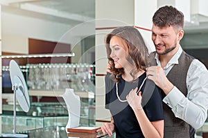 Young man helping his girlfriend with fitting necklace at the je