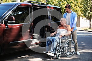 Young man helping patient in wheelchair to get into van
