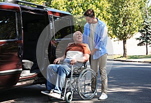 Young man helping patient in wheelchair to get into van