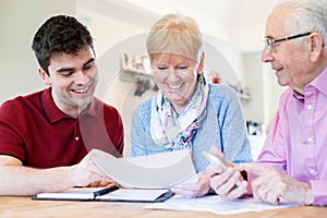 Young Man Helping Senior Couple With Financial Paperwork At Home