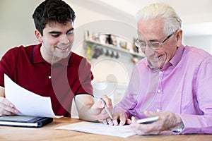 Young Man Helping Senior Neighbor With Paperwork At Home