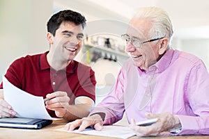 Young Man Helping Senior Neighbor With Paperwork At Home