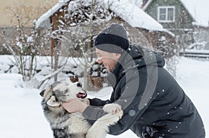 Young man with her dog husky outdoor on winter background. Active and happy man playing with dog, caressing and training