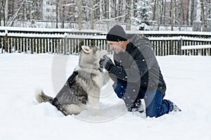 Young man with her dog husky outdoor on winter background. Active and happy man playing with dog, caressing and training