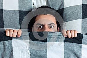 Young man hiding in bed under the blanket