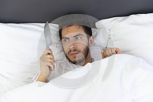 A young man is hiding in bed under a blanket at home