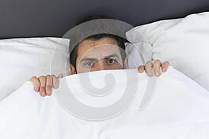 A young man is hiding in bed under a blanket at home