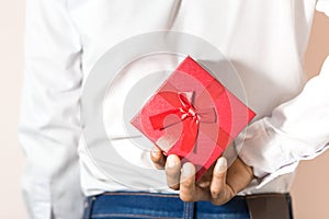 Young man hiding red gift box behind his back