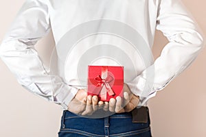 Young man hiding red gift box behind his back