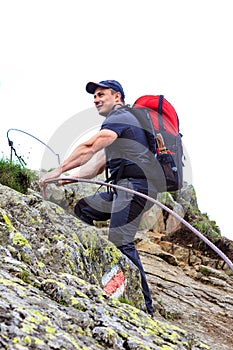 Young man hiking on difficult mountain trail with hanging cable