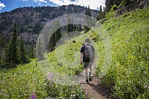 Young Man hiking on a high mountain trail walking towards the summit.