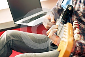 Casually dressed young man with guitar playing songs in the room at home. Online guitar lessons concept. Male guitarist practicing