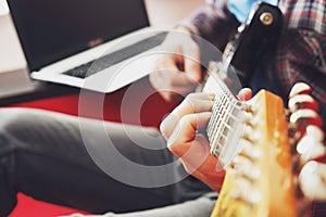 Casually dressed young man with guitar playing songs in the room at home. Online guitar lessons concept. Male guitarist practicing