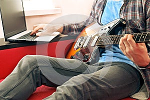 Casually dressed young man with guitar playing songs in the room at home. Online guitar lessons concept. Male guitarist practicing